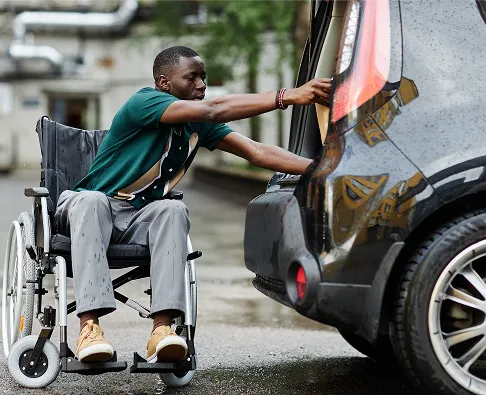 Person in a wheelchair next to a vehicle with an accessible parking permit